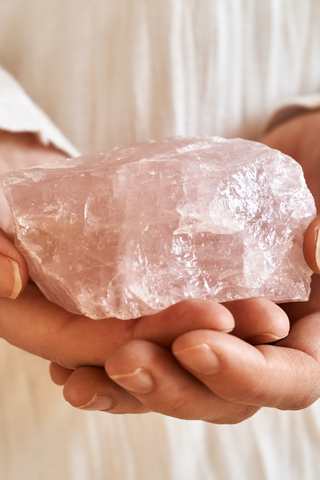 Two hands holding a rough rose quartz gemstone
