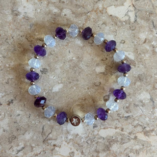 Beaded bracelet with purple and clear beads on a beige stone surface
